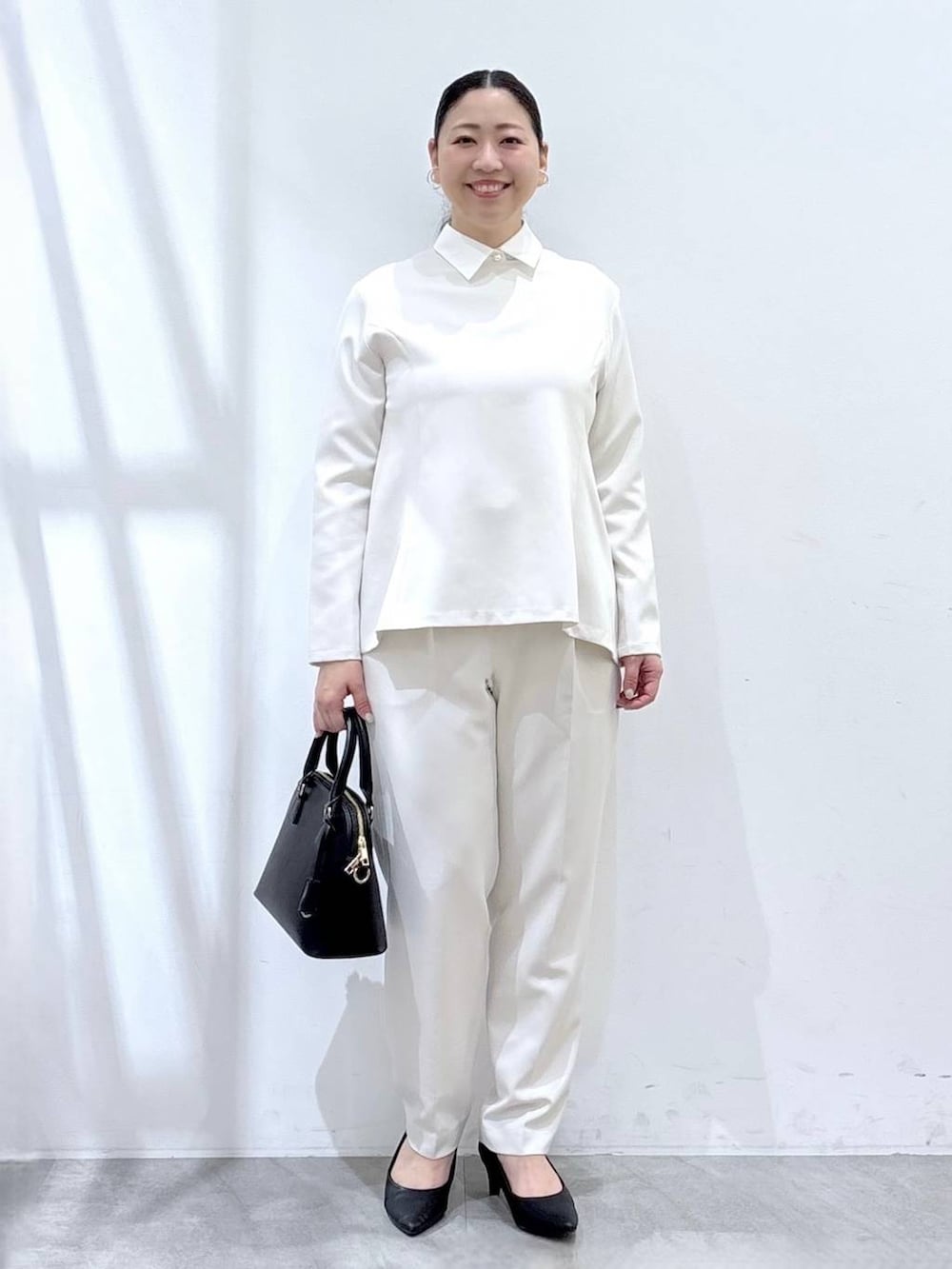 ブラック系のハンドバッグ、ホワイト系のシャツ/ブラウス、ホワイト系のスラックスを着用したレディースの春コーディネートの2枚目の写真