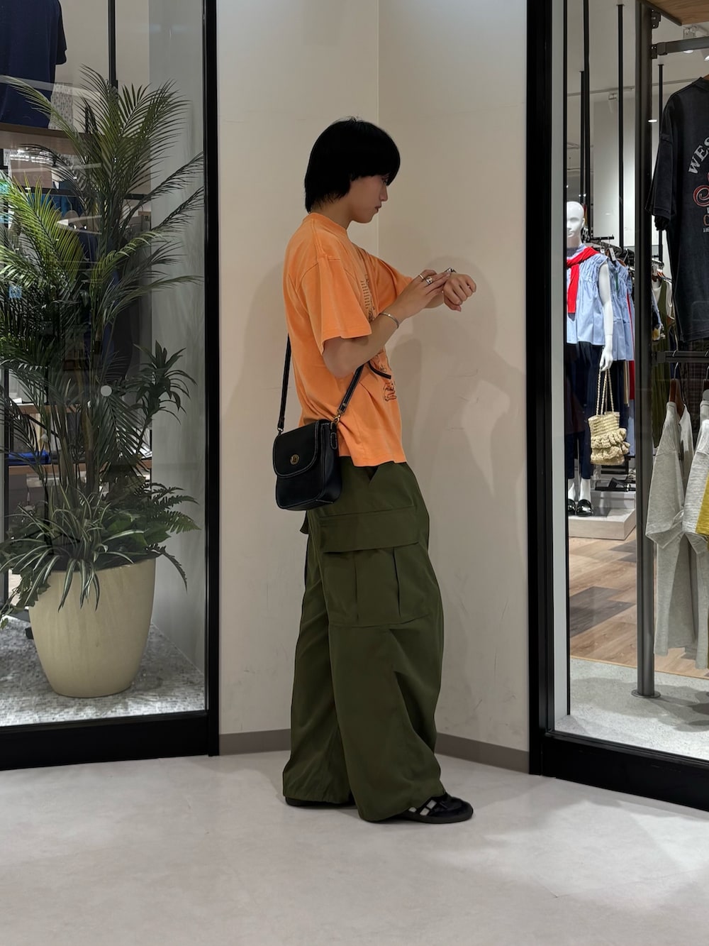 グリーン系のカーゴパンツ、オレンジ系のTシャツ/カットソー、ブラック系のショルダーバッグを着用したメンズの夏コーディネートの2枚目の写真