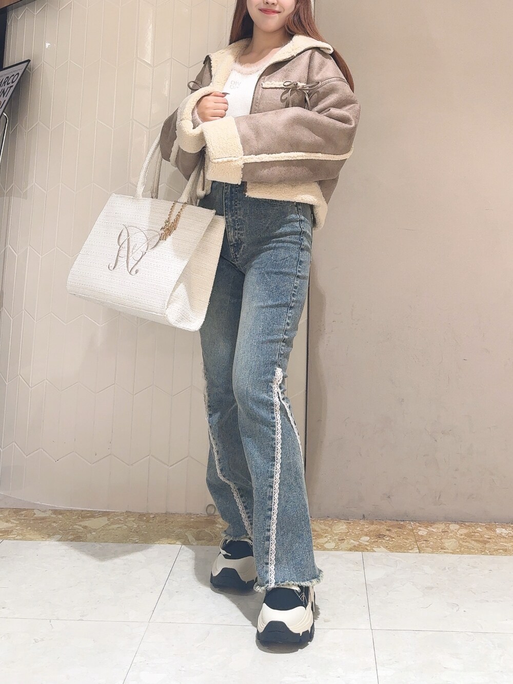 ホワイト系のニット/セーター、ブラウン系のブルゾン、ブルー系のデニムパンツを着用したレディースの秋コーディネートの3枚目の写真