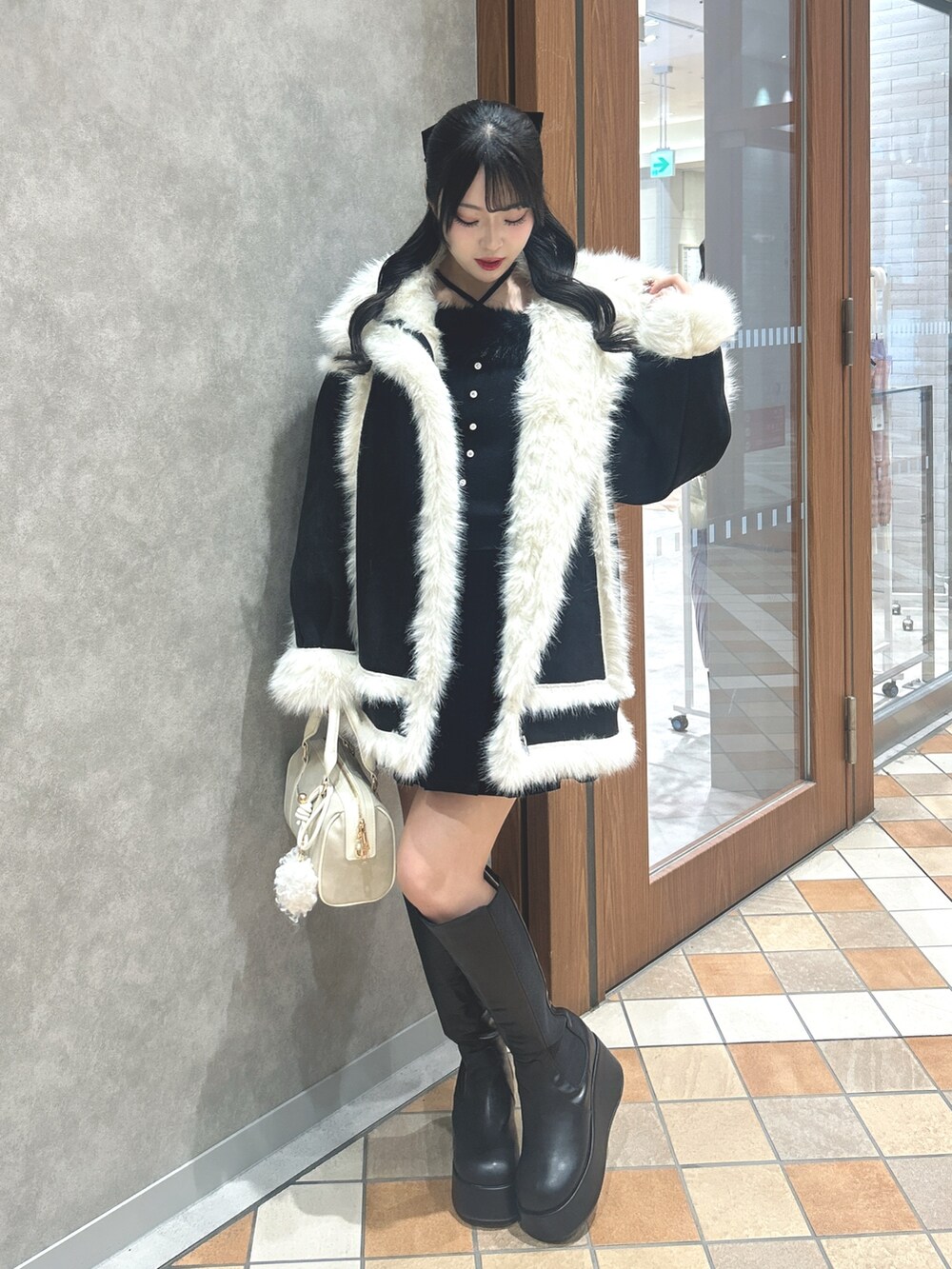 ブラック系のムートンコート、ブラック系のニット/セーター、ブラック系のスカートを着用したレディースの冬コーディネートの2枚目の写真