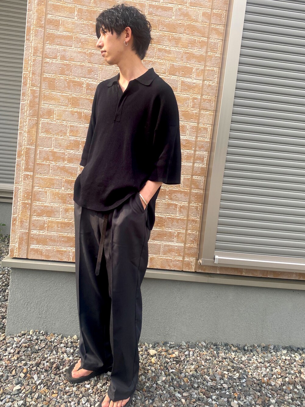 ブラック系のポロシャツ、グレー系のスラックス、ブラック系のサンダルを着用したメンズの夏コーディネートの2枚目の写真