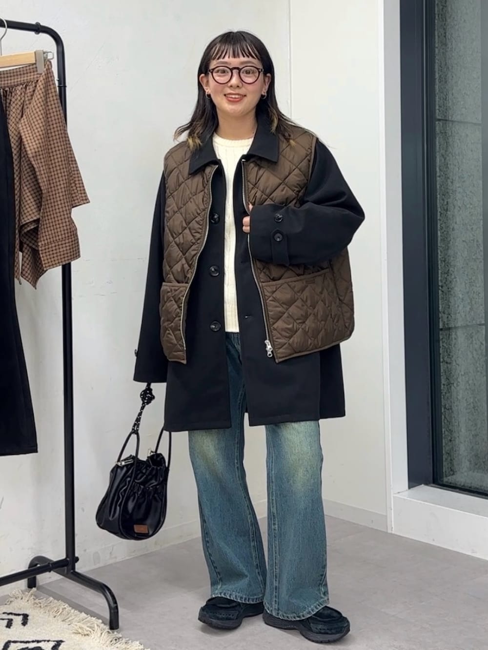 ブラック系のその他アウター、ブラック系のショルダーバッグ、ブルー系のデニムパンツを着用したレディースの秋コーディネートの2枚目の写真