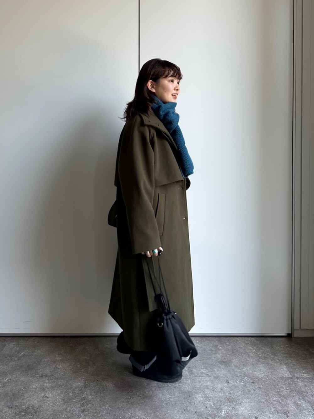 グリーン系のステンカラーコート、グレー系のスウェット、ブルー系のデニムパンツを着用したレディースの冬コーディネートの3枚目の写真