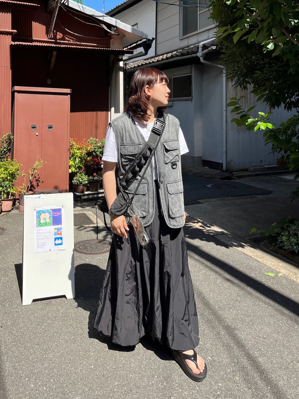 ブラック系のベスト、ブラック系のスカート、ブラック系のショルダーバッグを着用したレディースの夏コーディネートの2枚目の写真