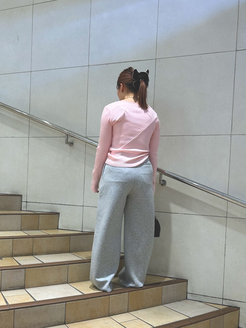 ピンク系のニット/セーター、グレー系のスラックス、ブラック系のハンドバッグを着用したレディースの春コーディネートの2枚目の写真