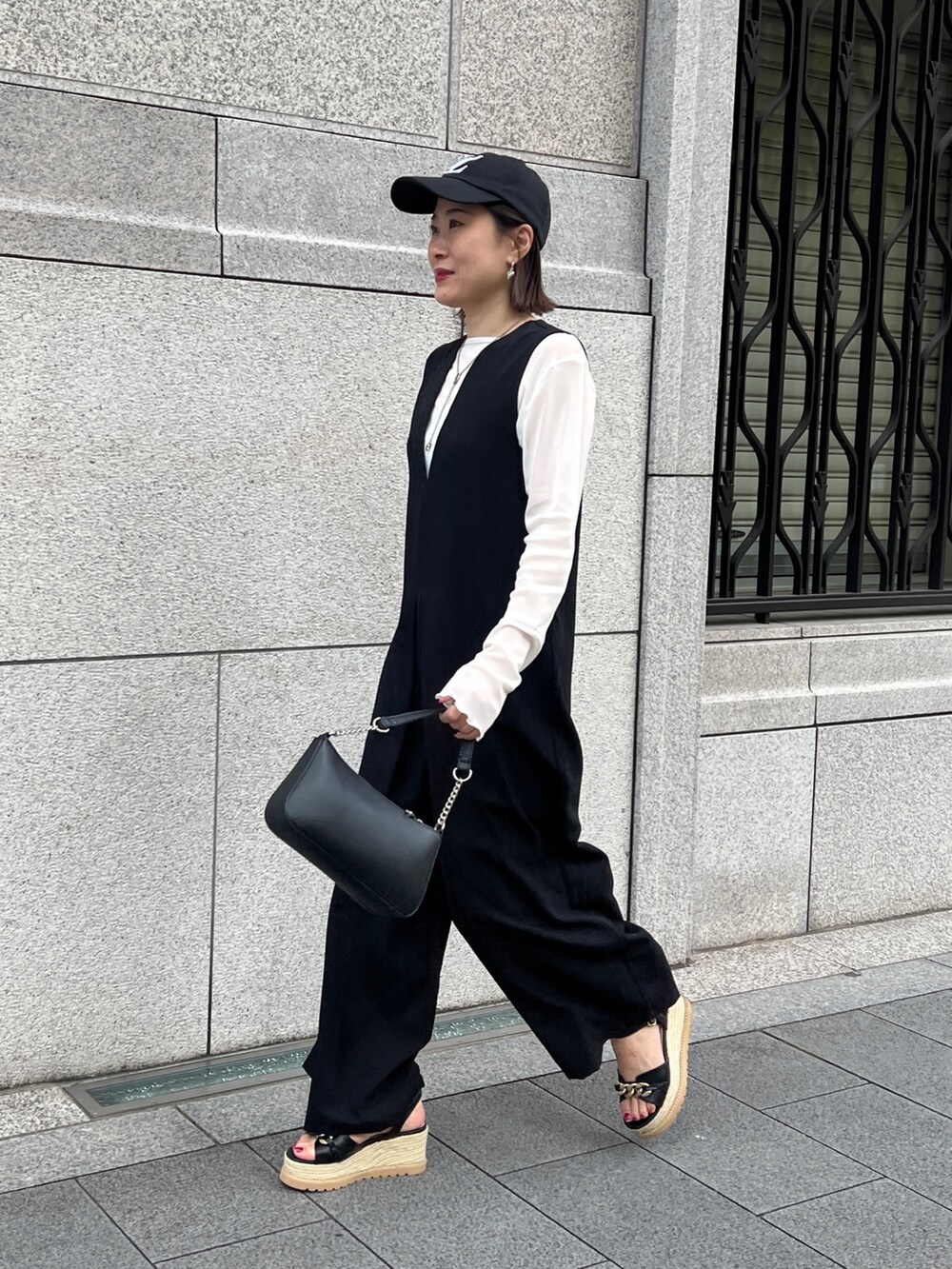 ブラック系のつなぎ/オールインワン、ホワイト系のTシャツ/カットソー、ブラック系のサンダルを着用したレディースの春コーディネートの2枚目の写真