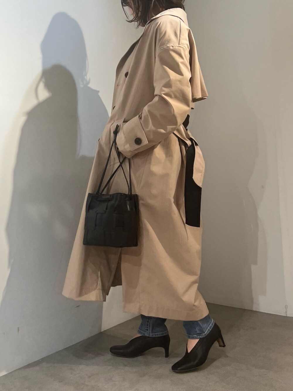 ベージュ系のトレンチコート、ブラック系のニット/セーター、ブルー系のデニムパンツを着用したレディースの冬コーディネートの2枚目の写真