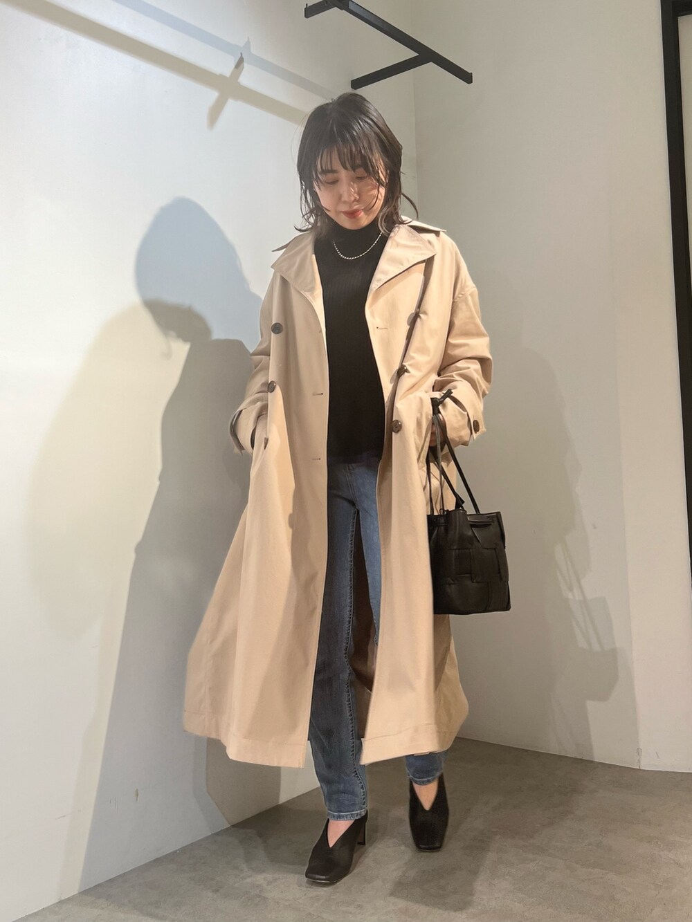 ベージュ系のトレンチコート、ブラック系のニット/セーター、ブルー系のデニムパンツを着用したレディースの冬コーディネートの3枚目の写真