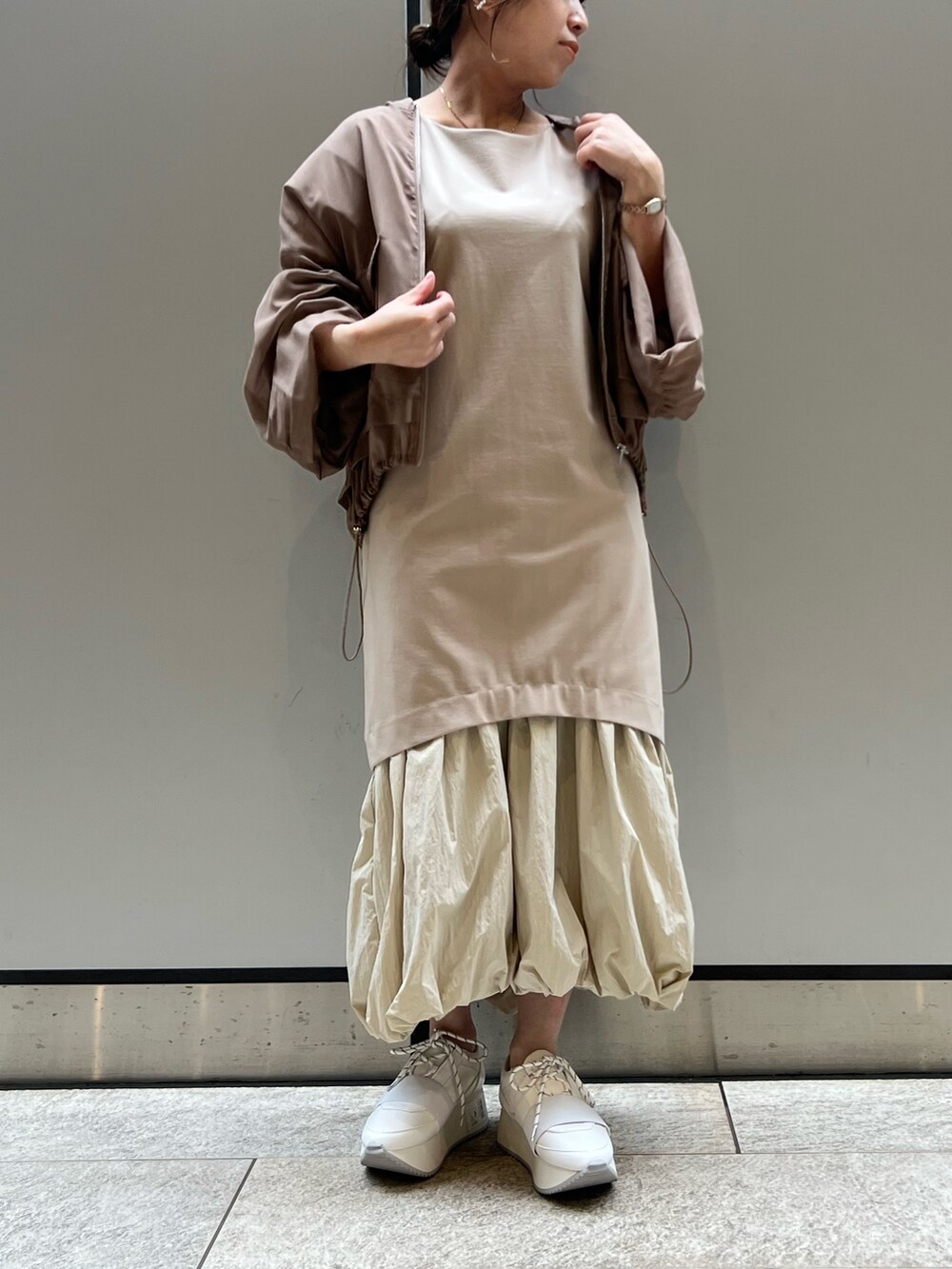 ベージュ系のワンピース、ホワイト系のスニーカー、ブラウン系のブルゾンを着用したレディースの春コーディネートの2枚目の写真
