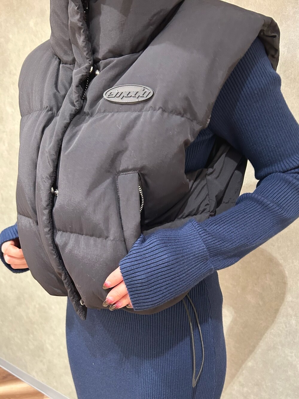 ブラック系のダウンベスト、ブルー系のワンピース、ブラック系のブーツを着用したレディースの秋コーディネートの4枚目の写真