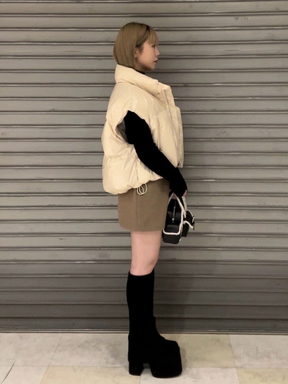 ホワイト系のダウンベスト、ブラック系のニット/セーター、ベージュ系のスカートを着用したレディースの秋コーディネートの3枚目の写真