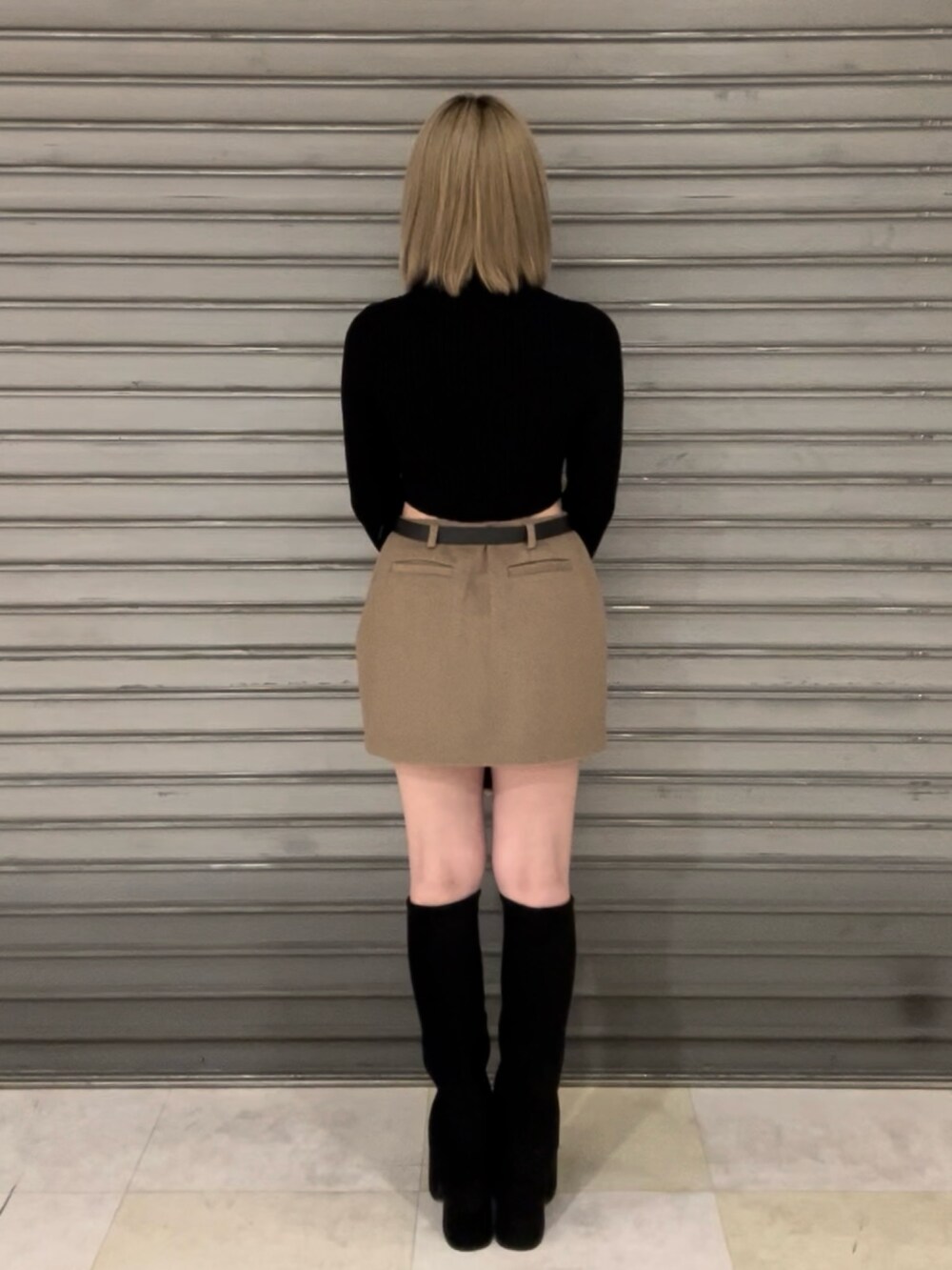 ホワイト系のダウンベスト、ブラック系のニット/セーター、ベージュ系のスカートを着用したレディースの秋コーディネートの6枚目の写真