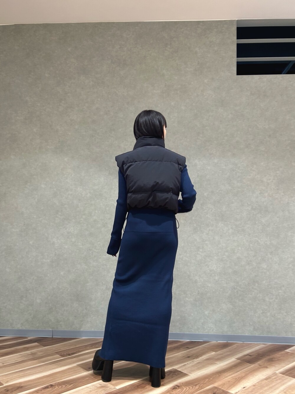 ブラック系のダウンベスト、ブルー系のワンピース、ブラック系のブーツを着用したレディースの秋コーディネートの3枚目の写真