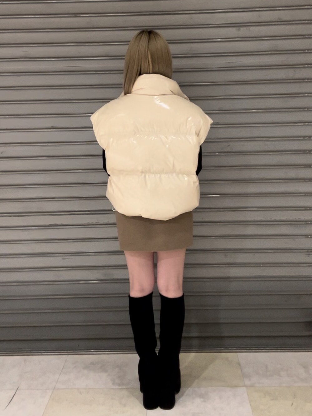 ホワイト系のダウンベスト、ブラック系のニット/セーター、ベージュ系のスカートを着用したレディースの秋コーディネートの5枚目の写真