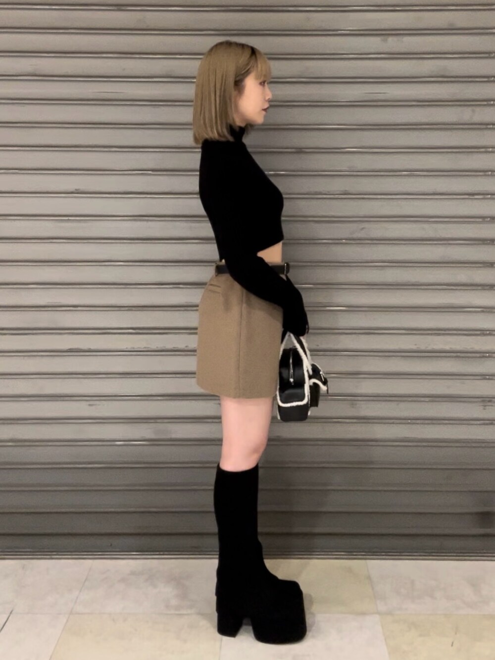 ホワイト系のダウンベスト、ブラック系のニット/セーター、ベージュ系のスカートを着用したレディースの秋コーディネートの4枚目の写真