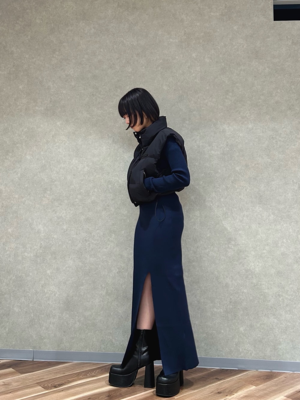 ブラック系のダウンベスト、ブルー系のワンピース、ブラック系のブーツを着用したレディースの秋コーディネートの2枚目の写真