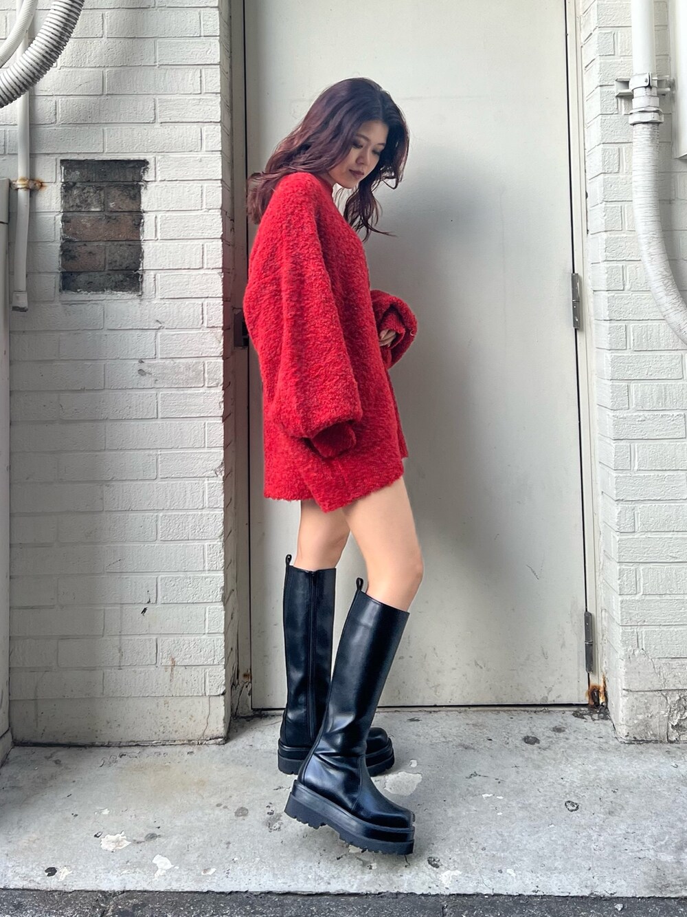 レッド系のニット/セーター、ブラック系のブーツを着用したレディースの冬コーディネートの2枚目の写真