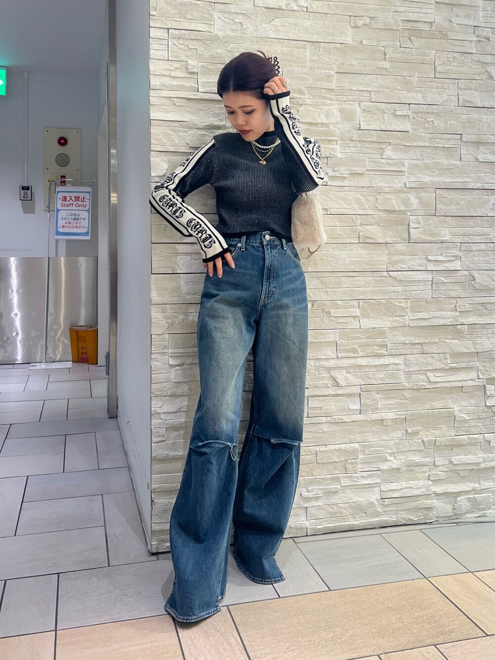 ブルー系のデニムパンツ、ホワイト系のショルダーバッグ、ブラック系のニット/セーターを着用したレディースの冬コーディネートの2枚目の写真