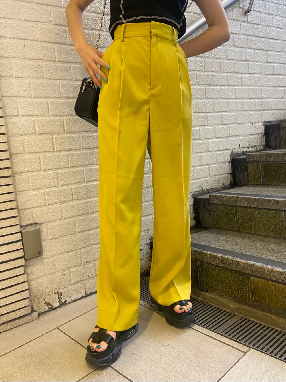 イエロー系のスラックス、ブラック系のショルダーバッグ、ブラック系のサンダルを着用したレディースの春コーディネートの6枚目の写真