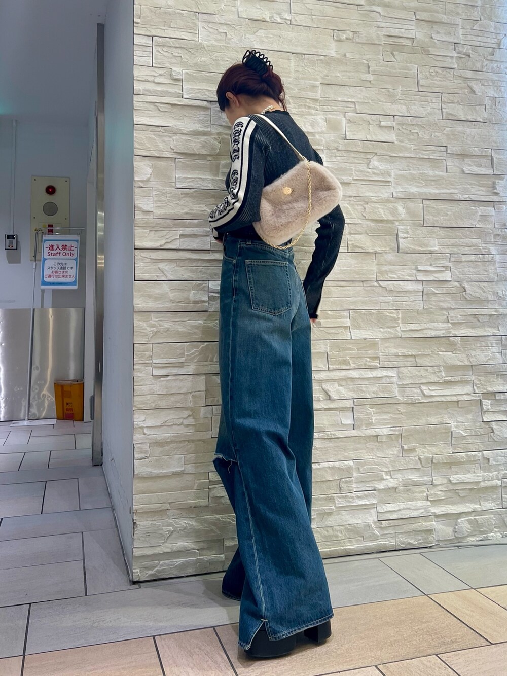 ブルー系のデニムパンツ、ホワイト系のショルダーバッグ、ブラック系のニット/セーターを着用したレディースの冬コーディネートの3枚目の写真