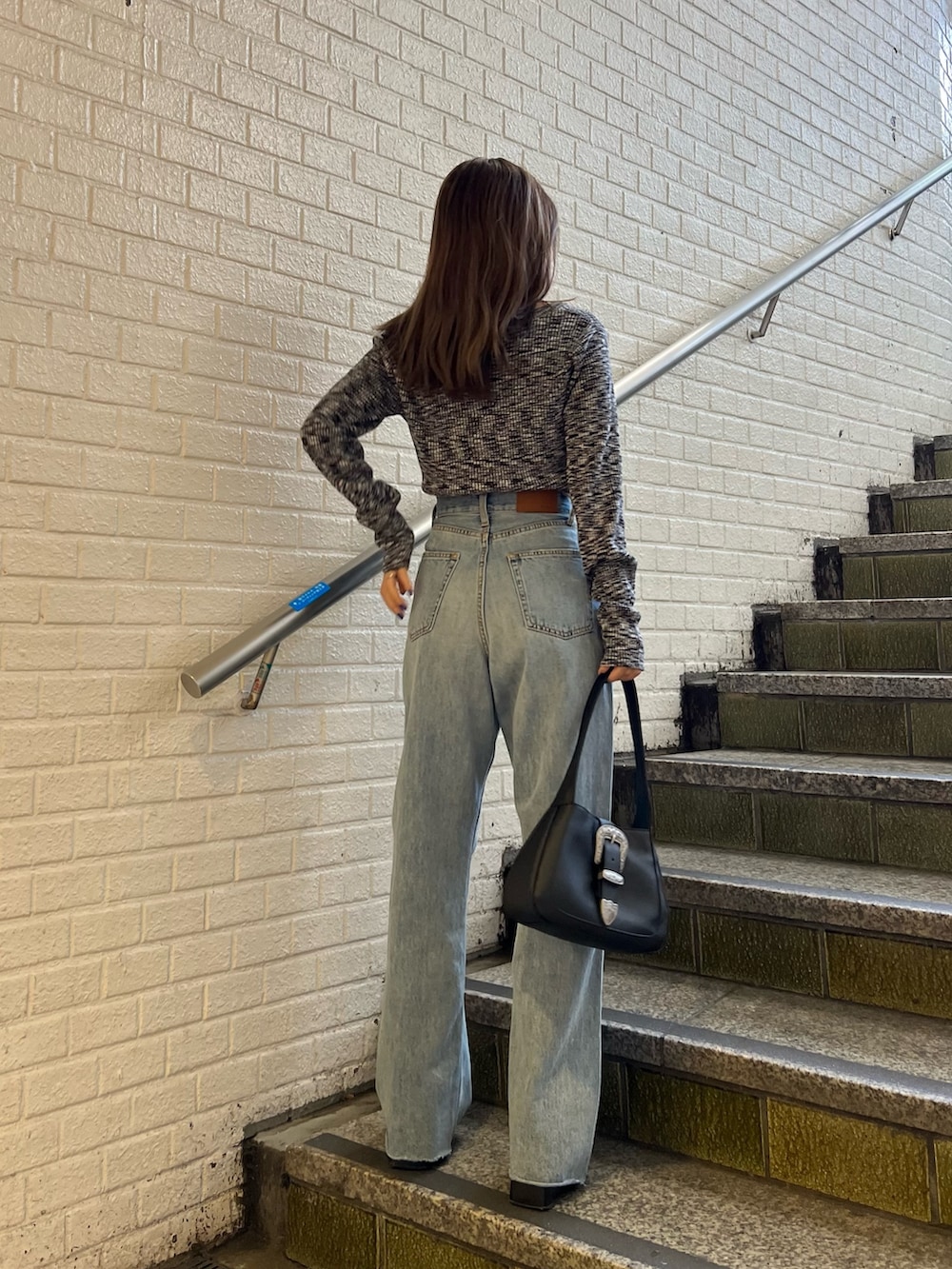 ブルー系のデニムパンツ、ブラック系のハンドバッグ、ブラック系のニット/セーターを着用したレディースの冬コーディネートの2枚目の写真