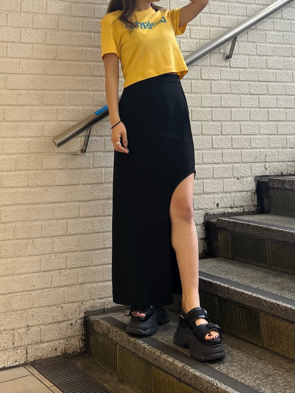 ブラック系のスカート、イエロー系のTシャツ/カットソー、ブラック系のサンダルを着用したレディースの春コーディネートの4枚目の写真