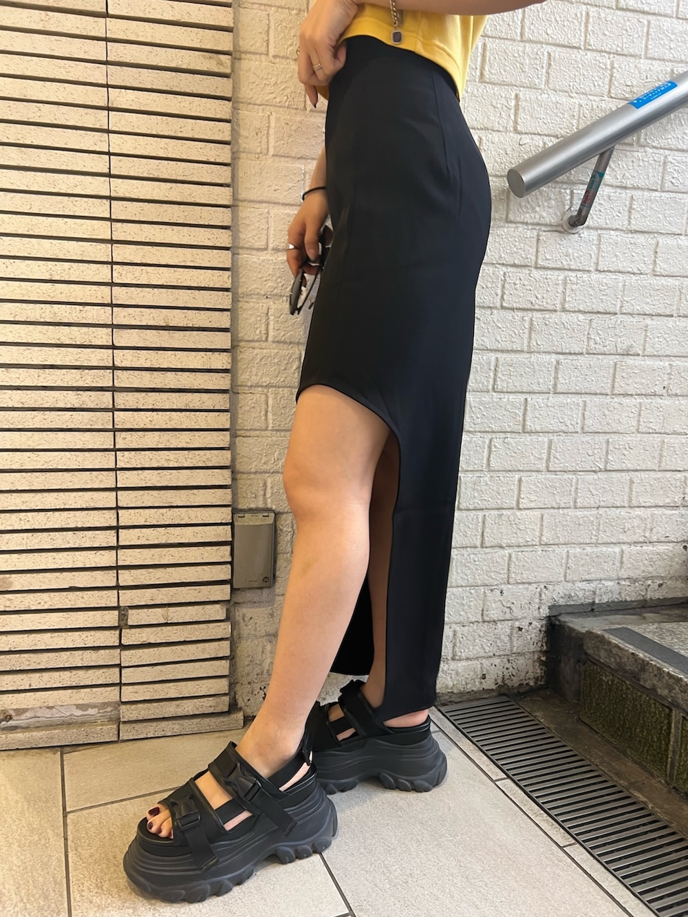 ブラック系のスカート、イエロー系のTシャツ/カットソー、ブラック系のサンダルを着用したレディースの春コーディネートの6枚目の写真