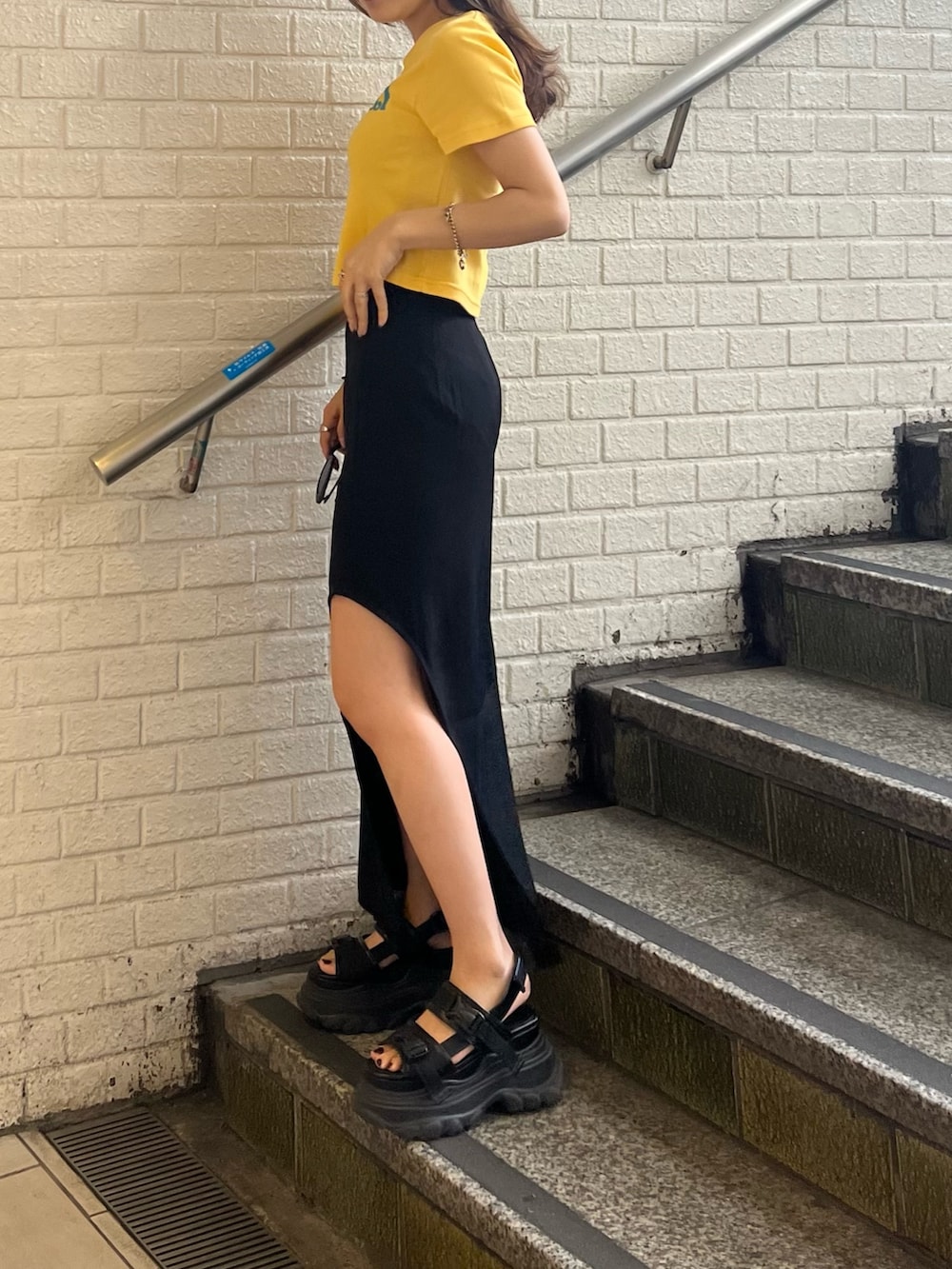 ブラック系のスカート、イエロー系のTシャツ/カットソー、ブラック系のサンダルを着用したレディースの春コーディネートの5枚目の写真