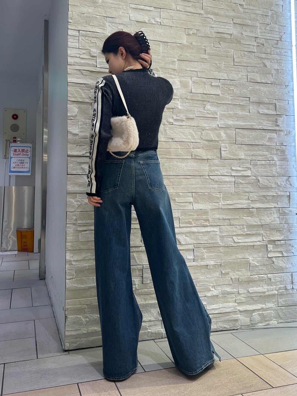 ブルー系のデニムパンツ、ホワイト系のショルダーバッグ、ブラック系のニット/セーターを着用したレディースの冬コーディネートの4枚目の写真