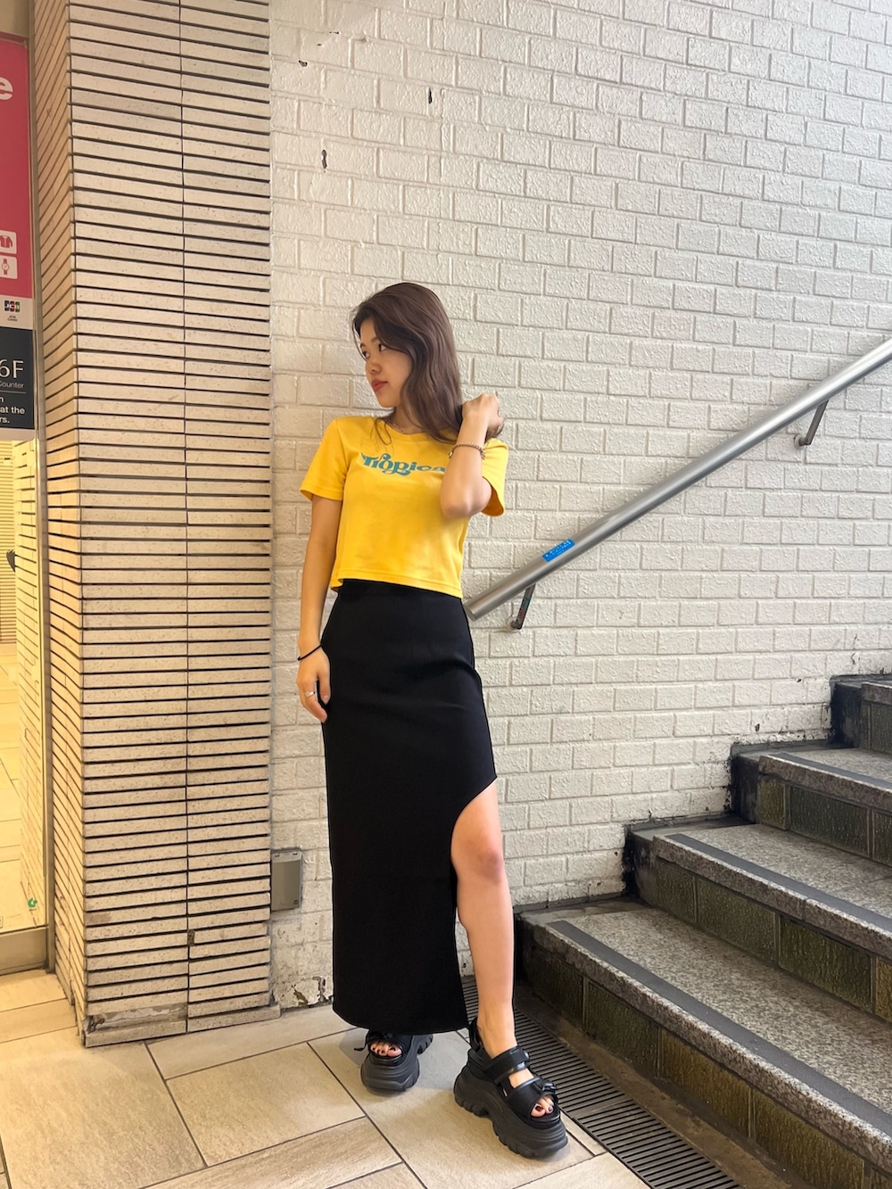 ブラック系のスカート、イエロー系のTシャツ/カットソー、ブラック系のサンダルを着用したレディースの春コーディネートの2枚目の写真