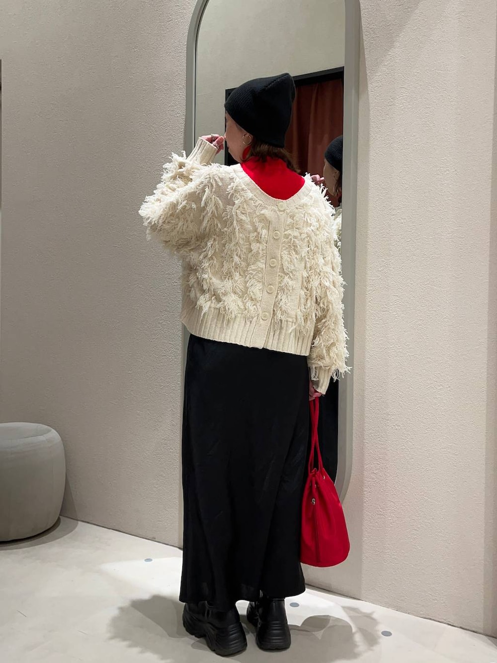 レッド系のニット/セーター、ブラック系のブーツ、ブラック系のスカートを着用したレディースの冬コーディネートの3枚目の写真