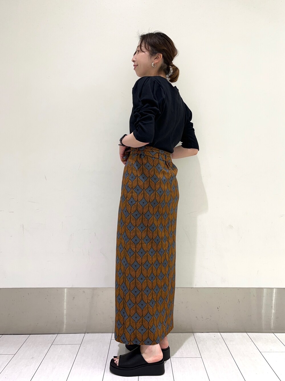 ブルー系のスカート、ブラック系のサンダル、ブラック系のTシャツ/カットソーを着用したレディースの夏コーディネートの2枚目の写真