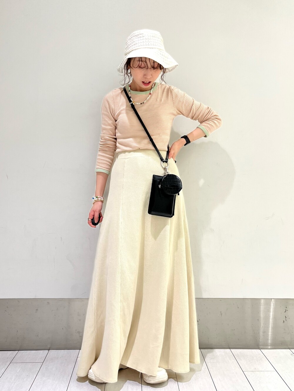 ブラック系のショルダーバッグ、ホワイト系のスカート、グリーン系のTシャツ/カットソーを着用したレディースの春コーディネートの2枚目の写真