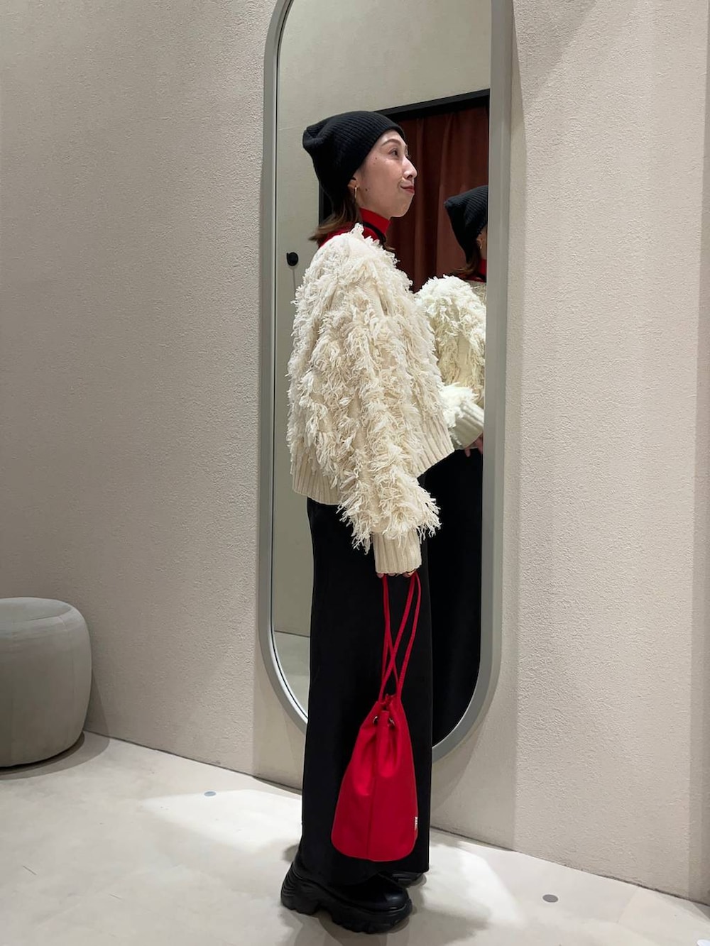 レッド系のニット/セーター、ブラック系のブーツ、ブラック系のスカートを着用したレディースの冬コーディネートの2枚目の写真