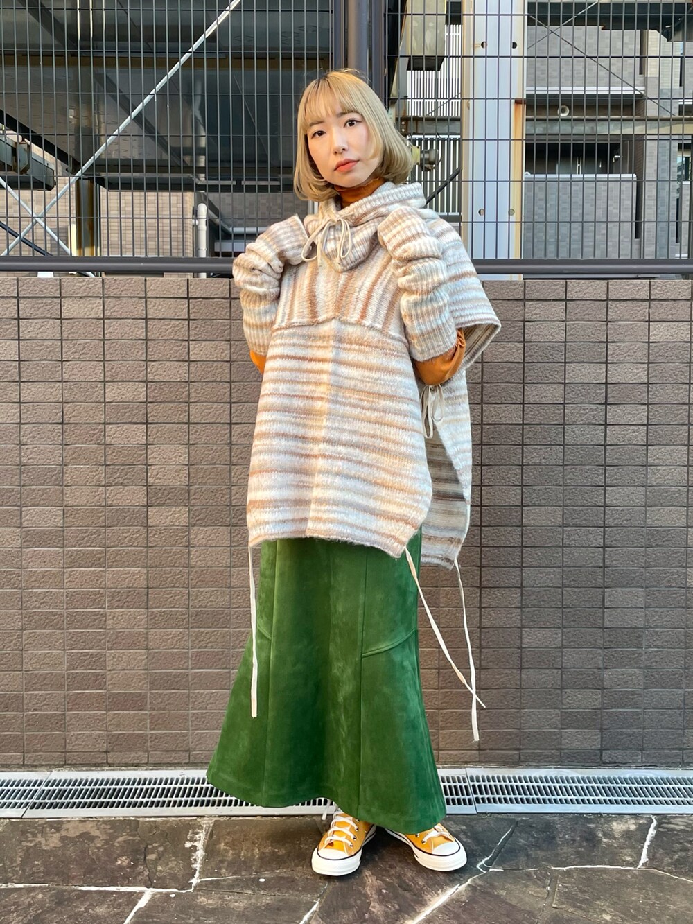 ベージュ系のニット/セーター、オレンジ系のTシャツ/カットソー、グリーン系のスカートを着用したレディースの秋コーディネートの2枚目の写真