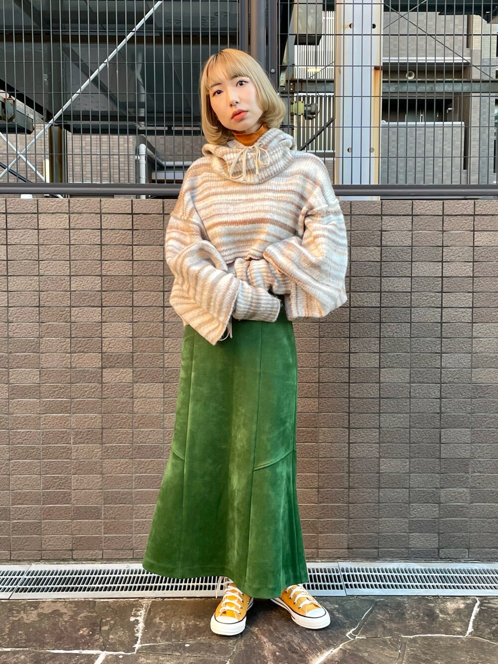 ベージュ系のニット/セーター、オレンジ系のTシャツ/カットソー、グリーン系のスカートを着用したレディースの秋コーディネートの3枚目の写真