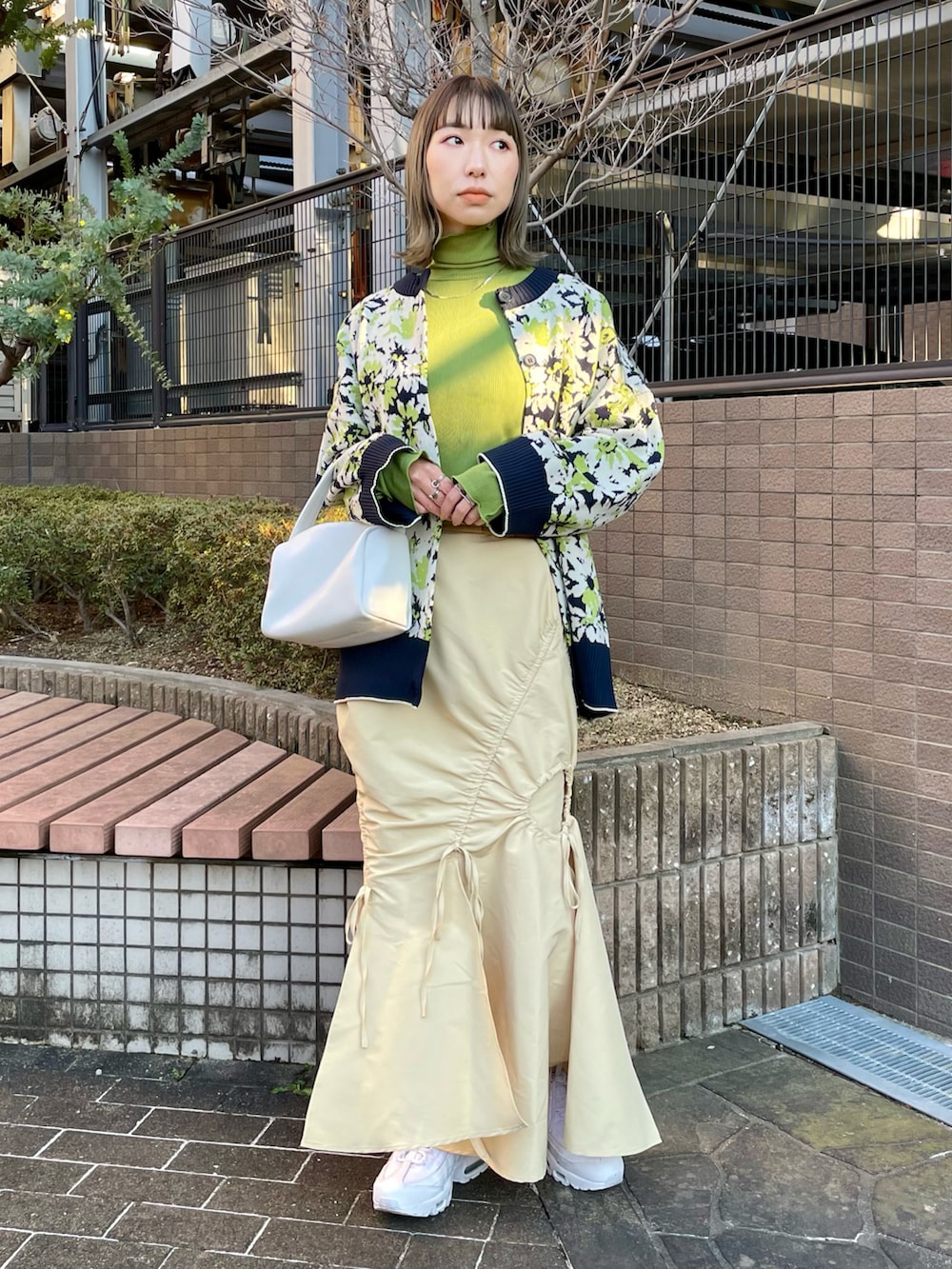 イエロー系のスカート、グリーン系のトレンチコート、グリーン系のカーディガン/ボレロを着用したレディースの冬コーディネートの2枚目の写真