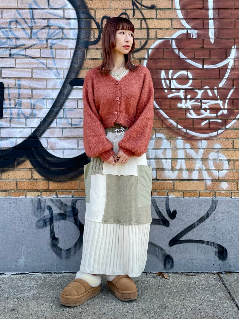 オレンジ系のカーディガン/ボレロ、ホワイト系のスカート、ホワイト系のTシャツ/カットソーを着用したレディースの冬コーディネートの2枚目の写真