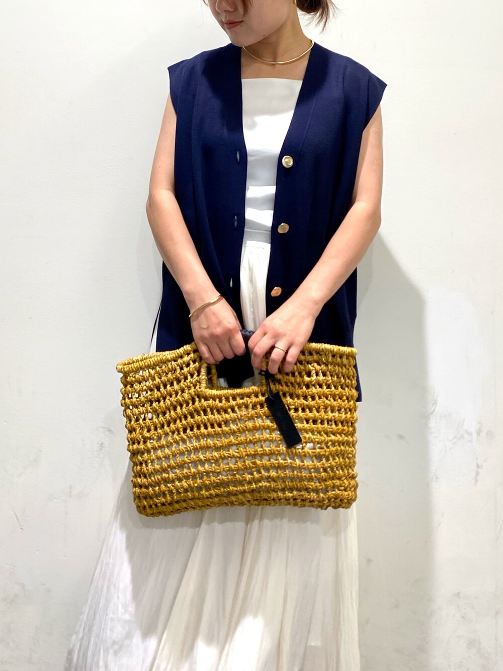 ベージュ系のかごバッグ、ブラウン系のサンダル、ブルー系のベストを着用したレディースの夏コーディネートの2枚目の写真