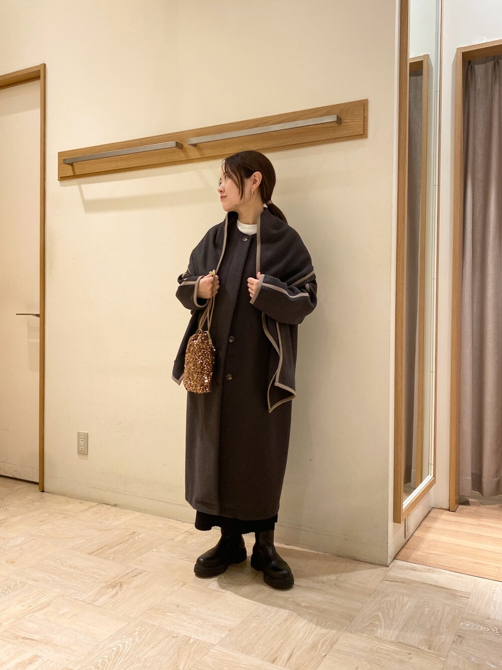 グレー系のノーカラーコート、ブラック系のブーツ、ゴールド系のショルダーバッグを着用したレディースの秋コーディネートの2枚目の写真