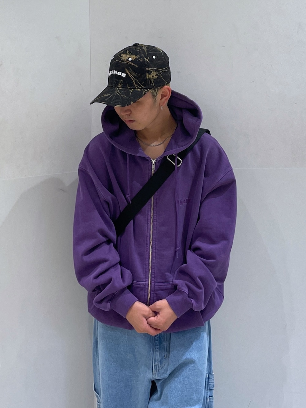 パープル系のパーカー、ブルー系のデニムパンツ、ブラック系のショルダーバッグを着用したメンズの秋コーディネートの5枚目の写真