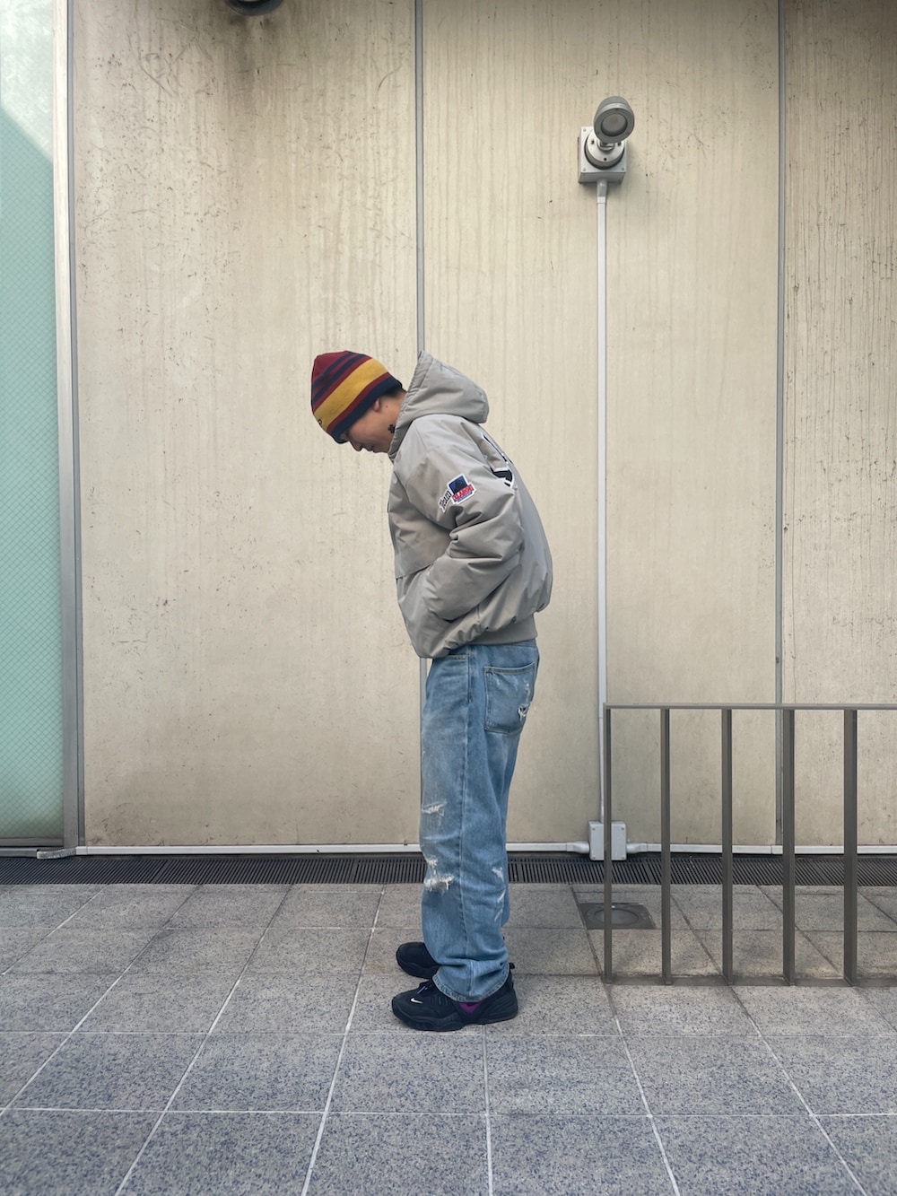 グレー系のナイロンジャケット、ブルー系のデニムパンツ、レッド系のニットキャップ/ビーニーを着用したメンズの冬コーディネートの2枚目の写真