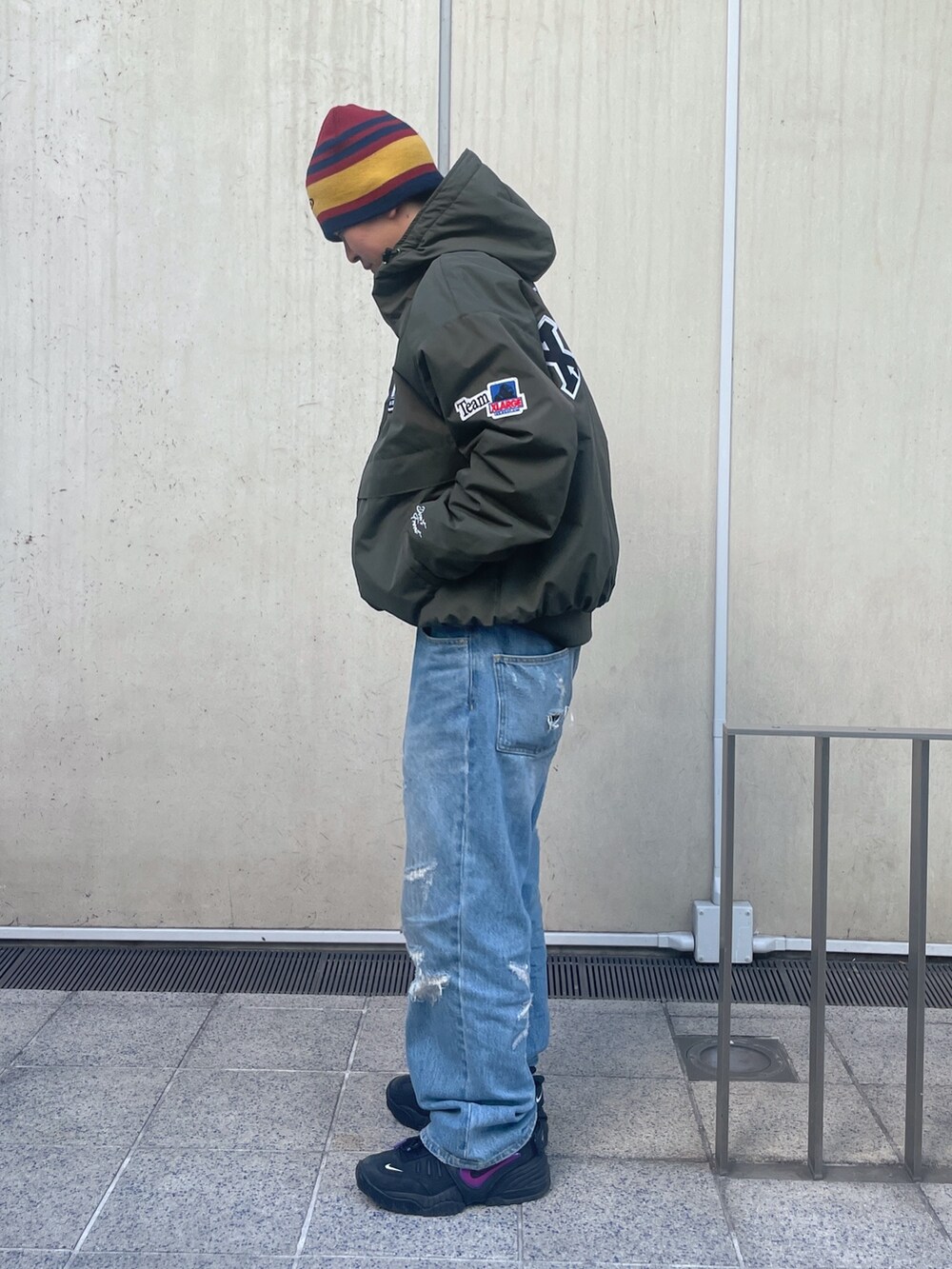 グリーン系のナイロンジャケット、ブルー系のデニムパンツ、レッド系のニットキャップ/ビーニーを着用したメンズの冬コーディネートの2枚目の写真