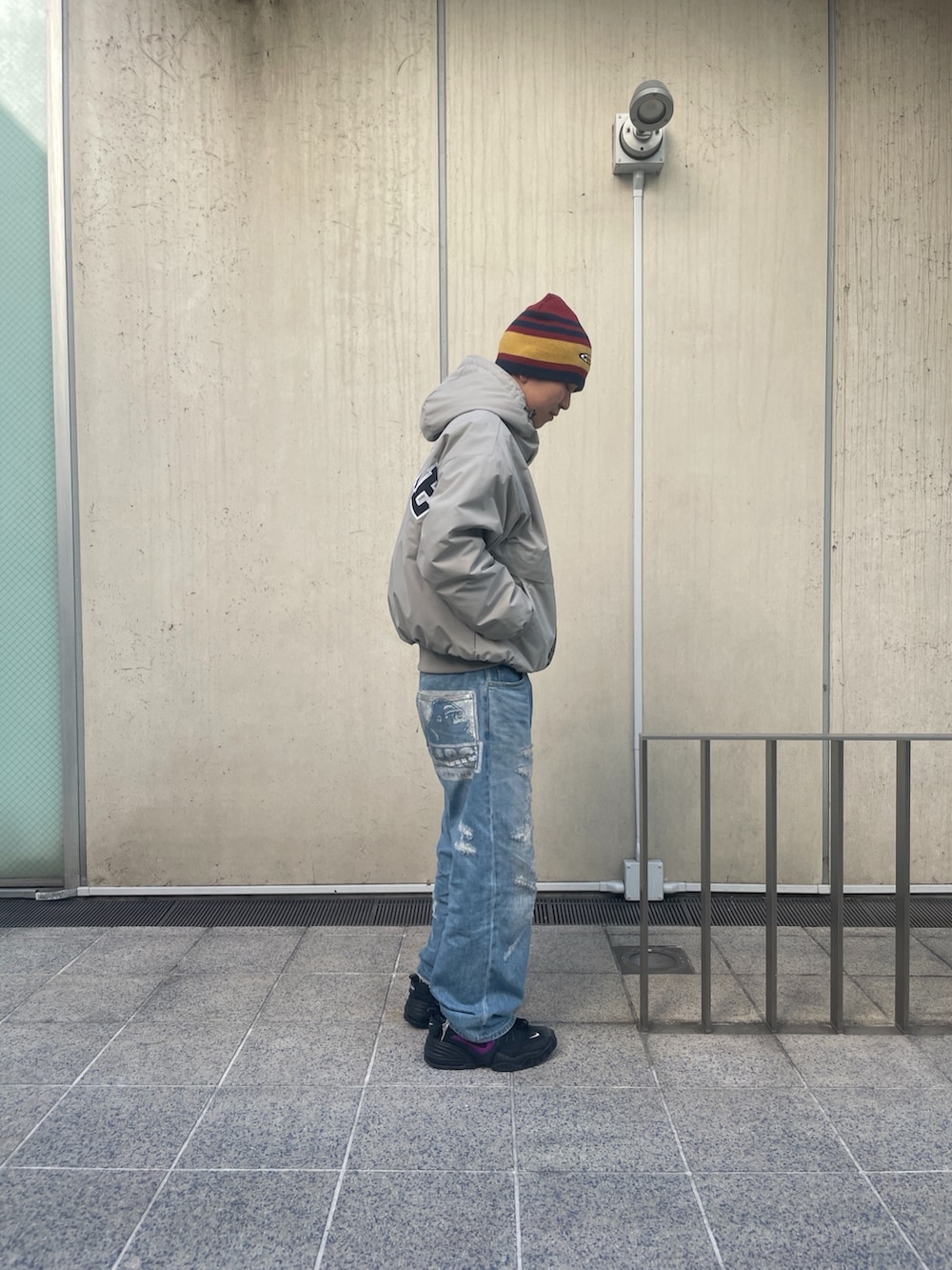 グレー系のナイロンジャケット、ブルー系のデニムパンツ、レッド系のニットキャップ/ビーニーを着用したメンズの冬コーディネートの5枚目の写真