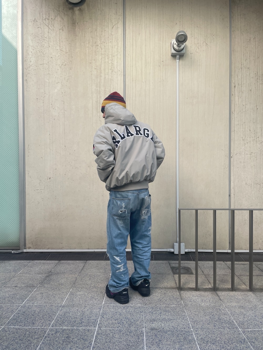 グレー系のナイロンジャケット、ブルー系のデニムパンツ、レッド系のニットキャップ/ビーニーを着用したメンズの冬コーディネートの3枚目の写真