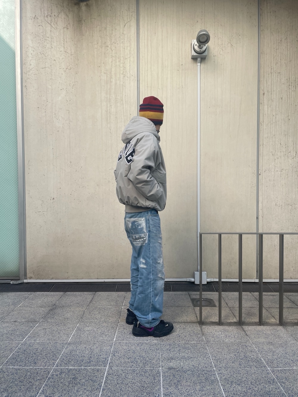 グレー系のナイロンジャケット、ブルー系のデニムパンツ、レッド系のニットキャップ/ビーニーを着用したメンズの冬コーディネートの4枚目の写真