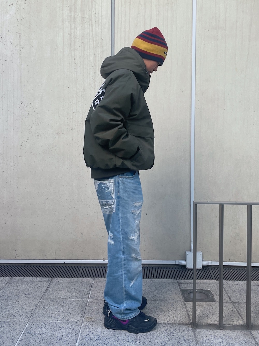 グリーン系のナイロンジャケット、ブルー系のデニムパンツ、レッド系のニットキャップ/ビーニーを着用したメンズの冬コーディネートの4枚目の写真