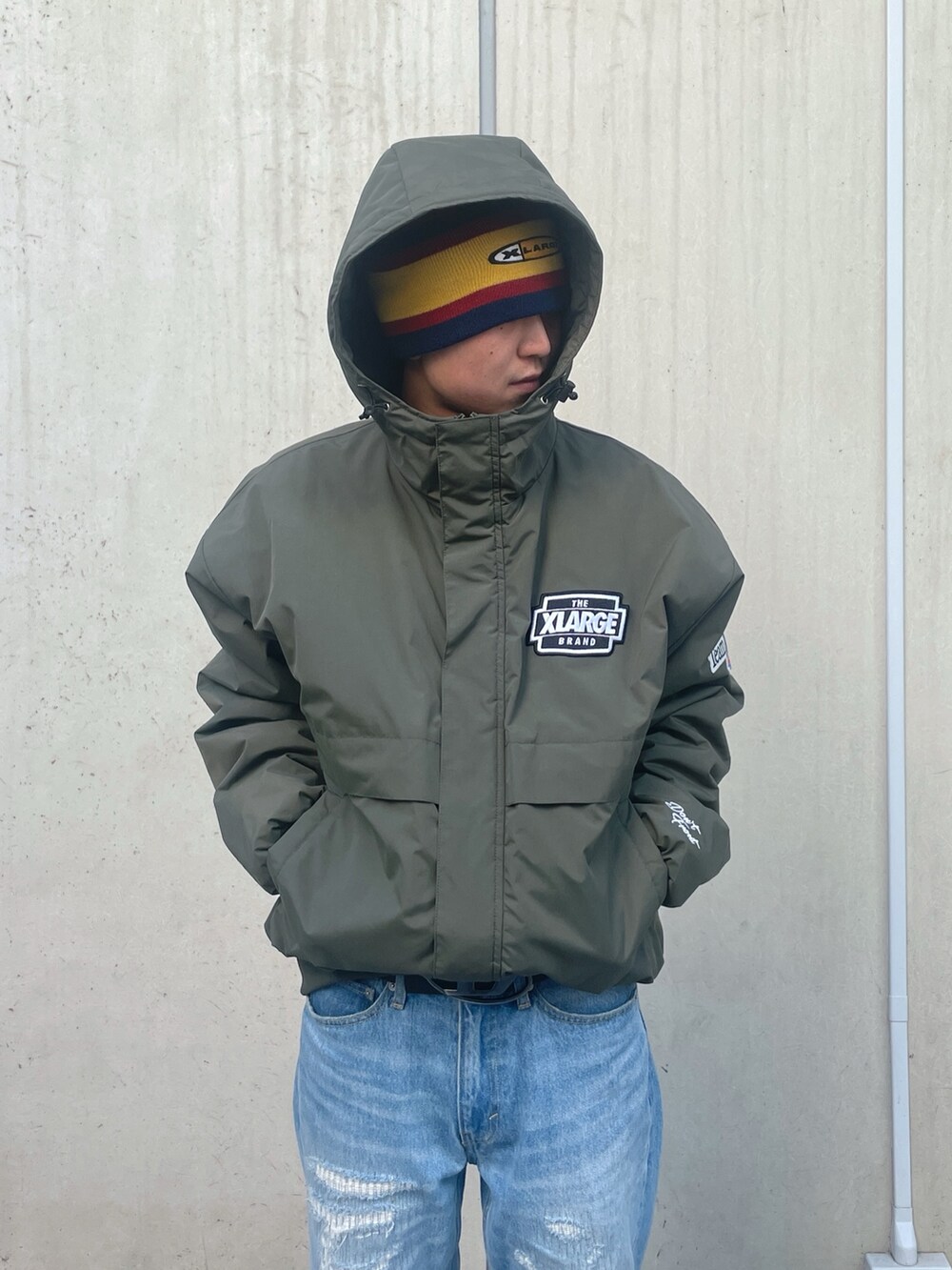 グリーン系のナイロンジャケット、ブルー系のデニムパンツ、レッド系のニットキャップ/ビーニーを着用したメンズの冬コーディネートの6枚目の写真