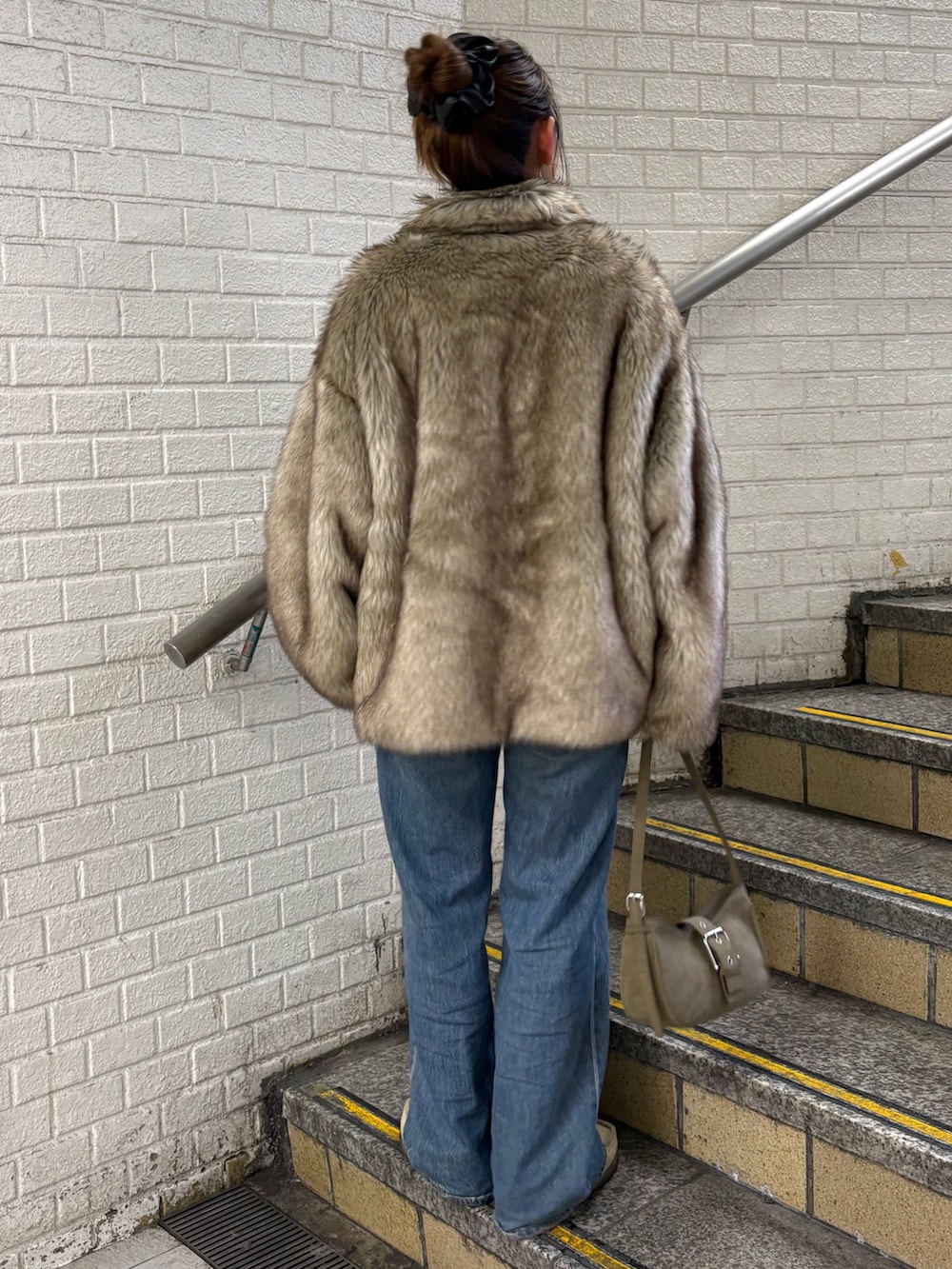 ベージュ系のダウンジャケット/コート、グリーン系のハンドバッグ、ブルー系のデニムパンツを着用したレディースの秋コーディネートの3枚目の写真