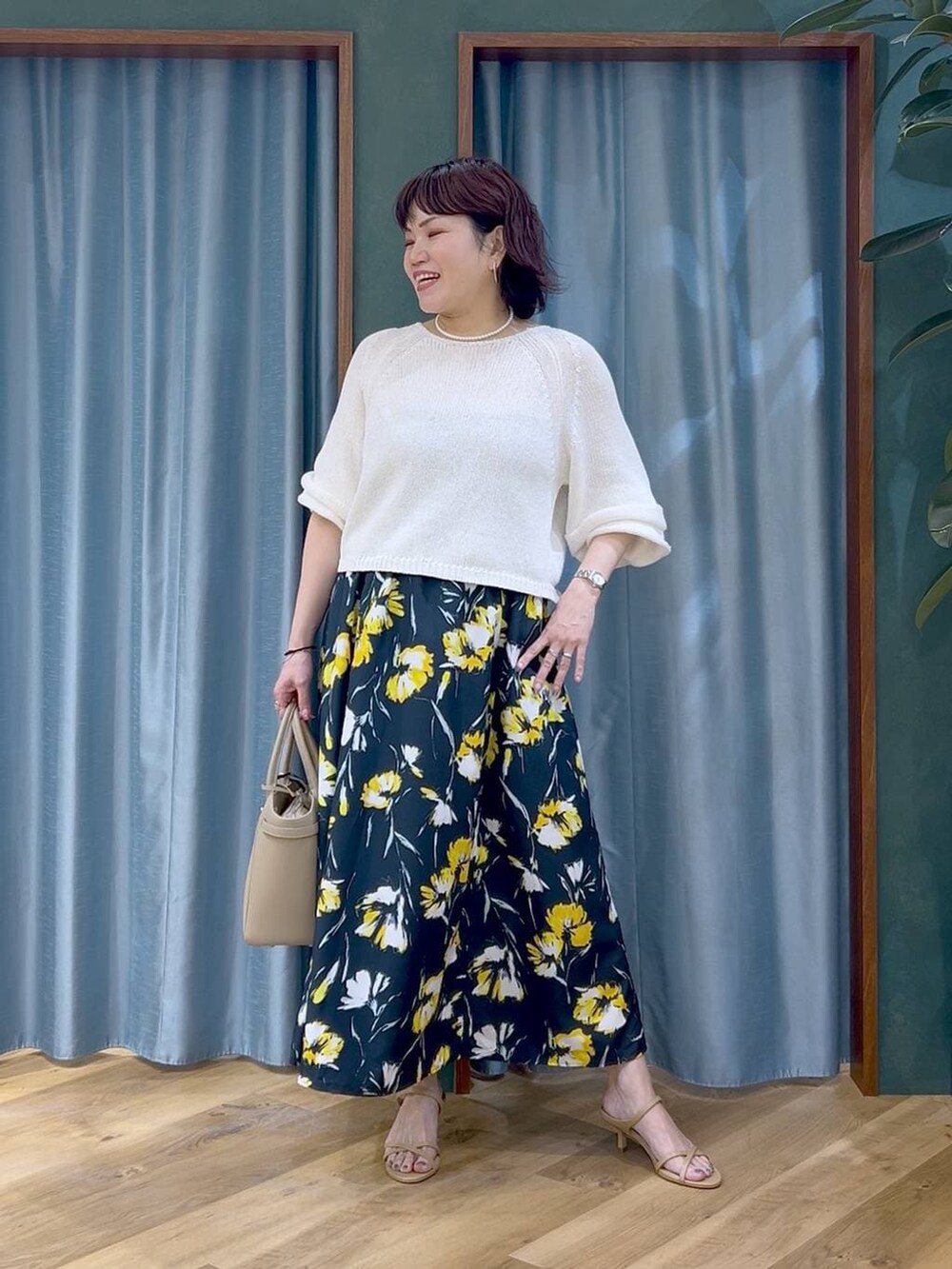 ホワイト系のニット/セーター、ブルー系のスカート、ベージュ系のハンドバッグを着用したレディースの春コーディネートの2枚目の写真